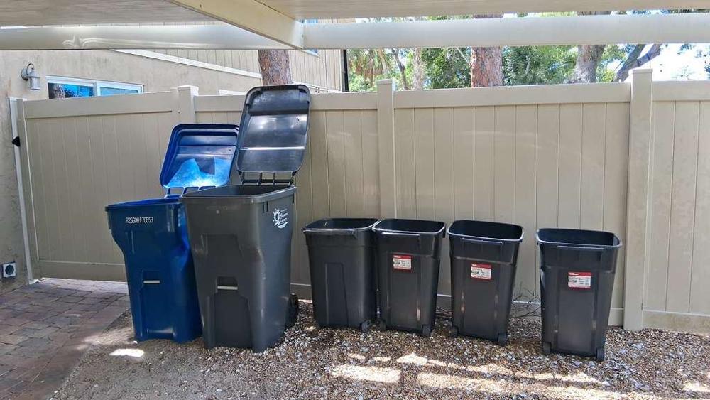 Botes de basura y reciclaje junto a una cerca